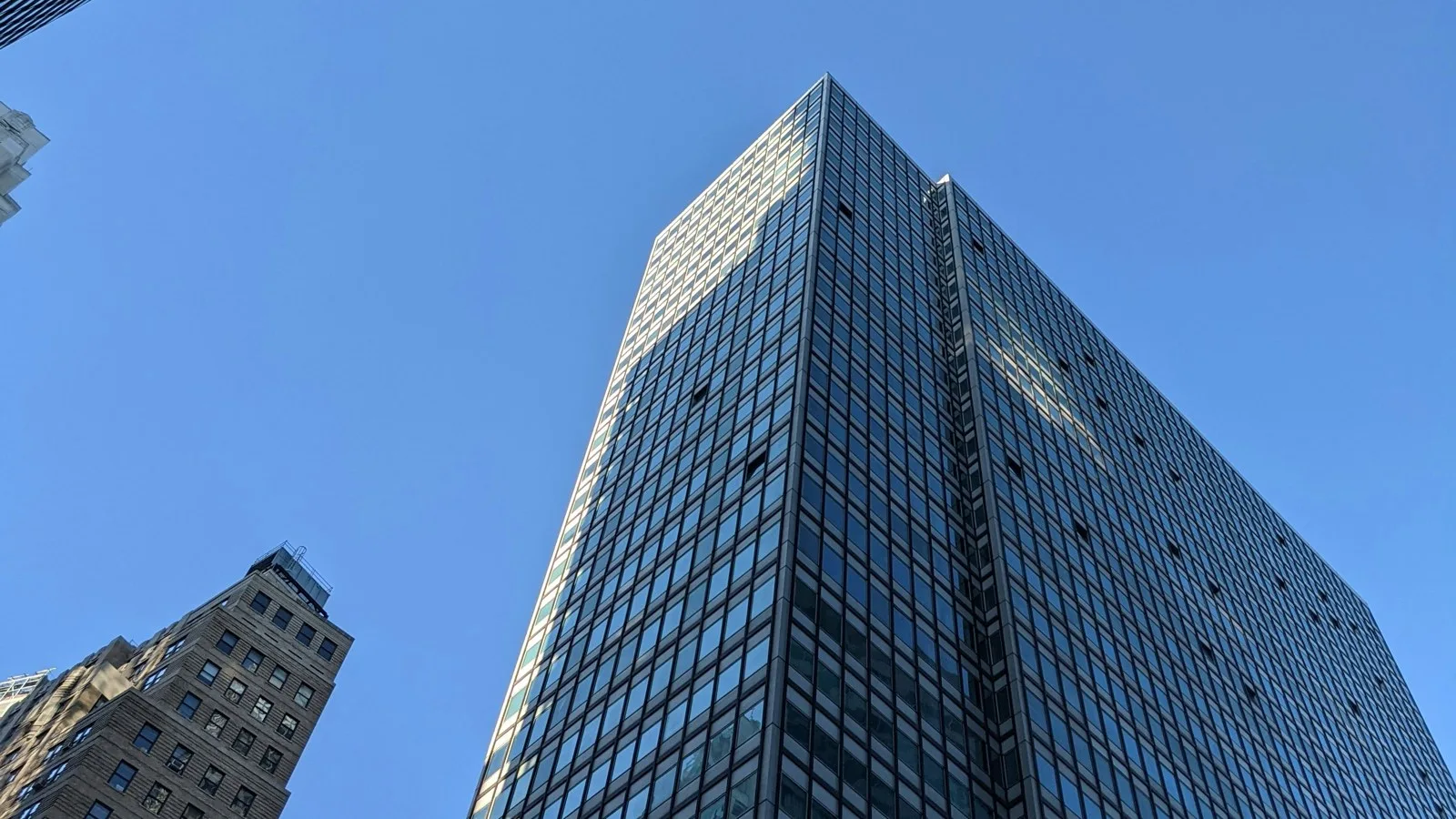 Glass office tower rising against a clear blue sky beside an older stone building