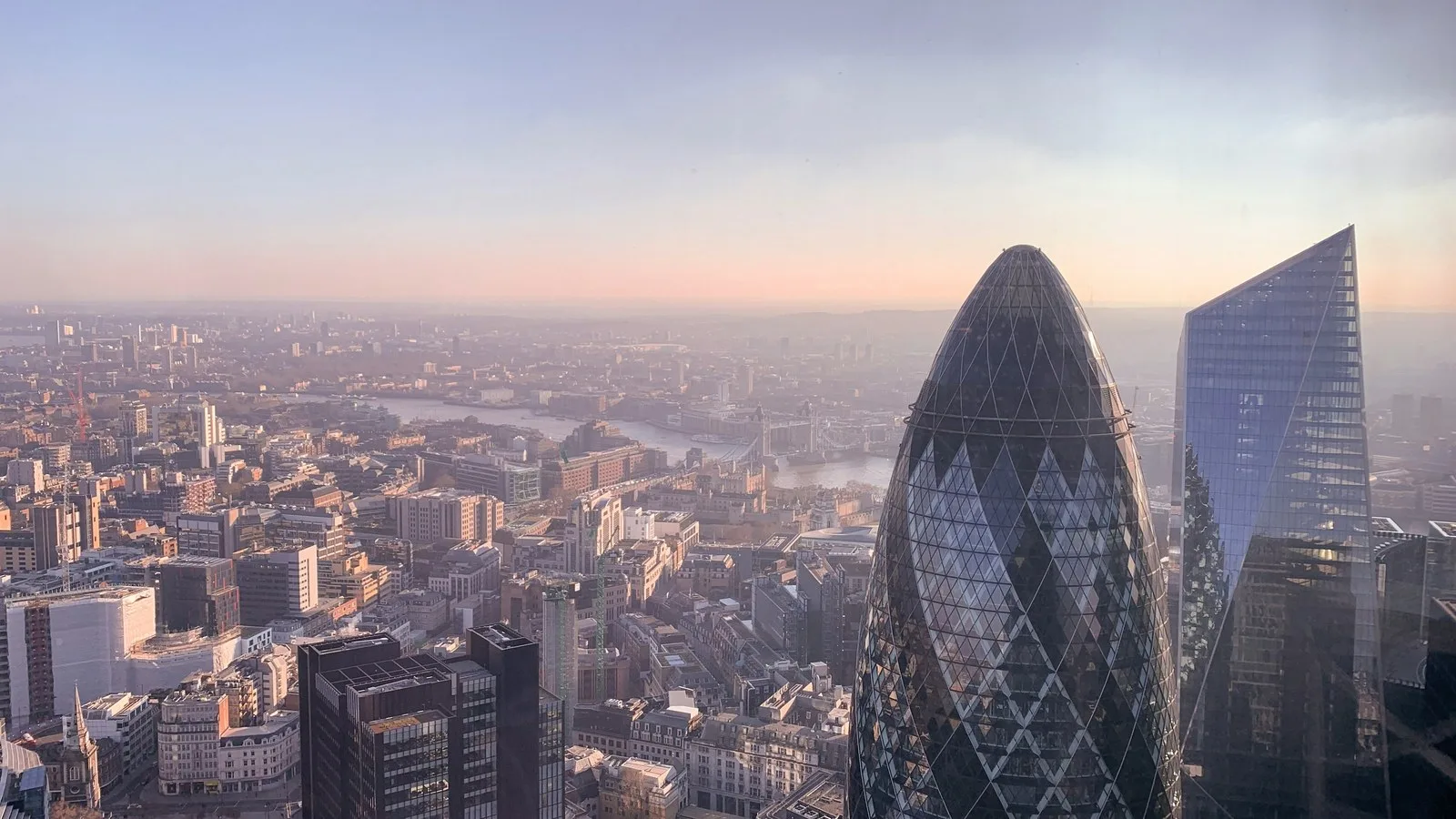 Aerial view of London at dusk with a glass tower in the foreground and the River Thames winding into the distance