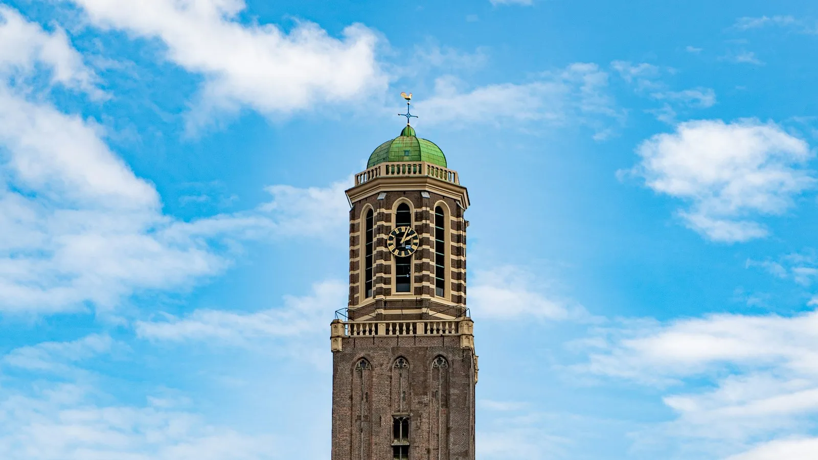 Brick clock tower with a green copper dome and gold weathercock rising into a blue sky with scattered white clouds in the Dutch city of Zwolle