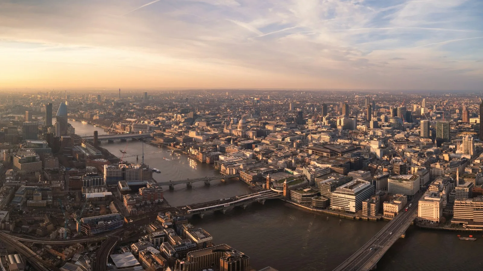 Aerial view of the River Thames and the City of London at sunset, with bridges and office buildings stretching toward the horizon