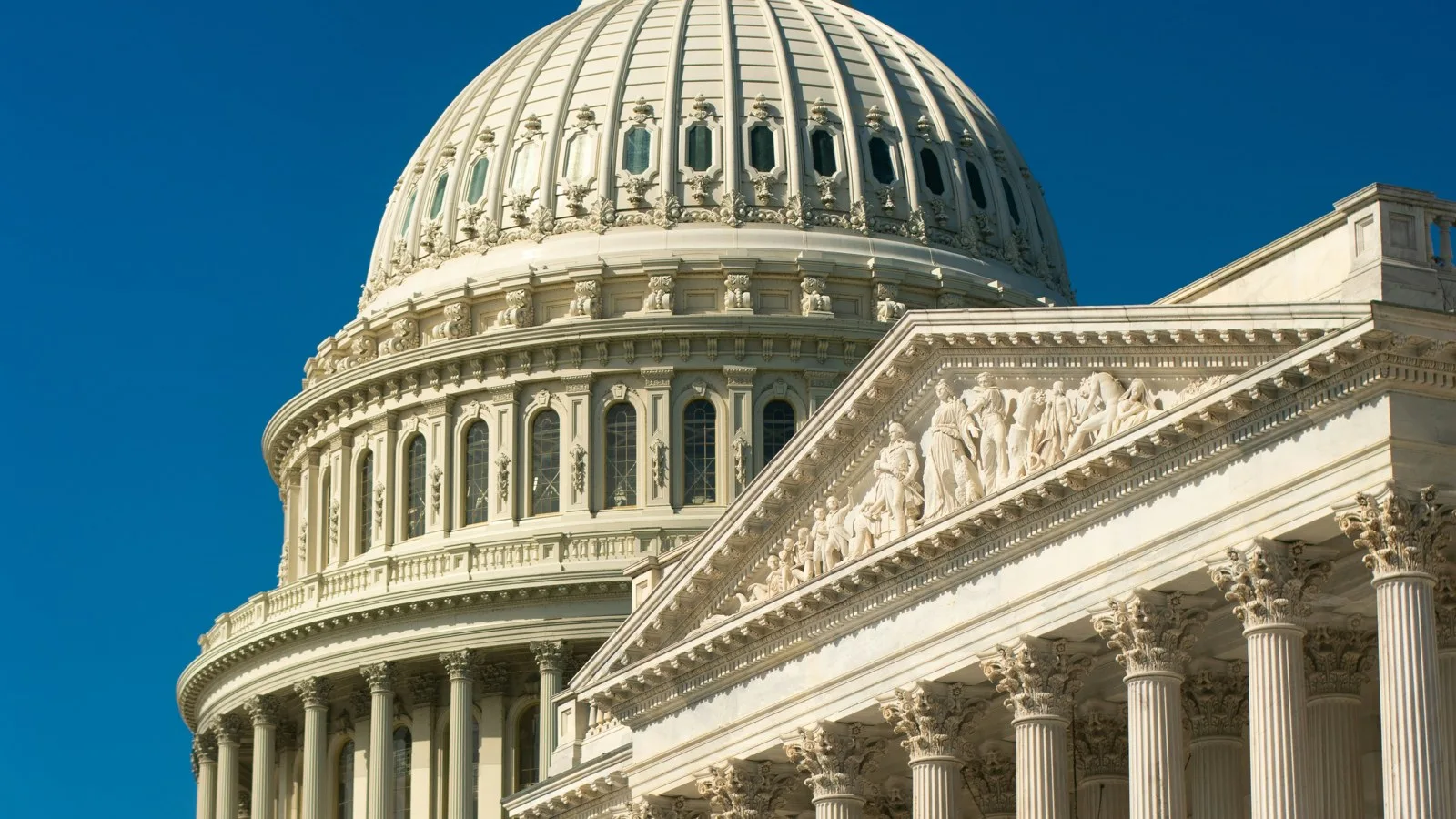 The white dome and columned east front of the US Capitol in Washington under a deep blue sky