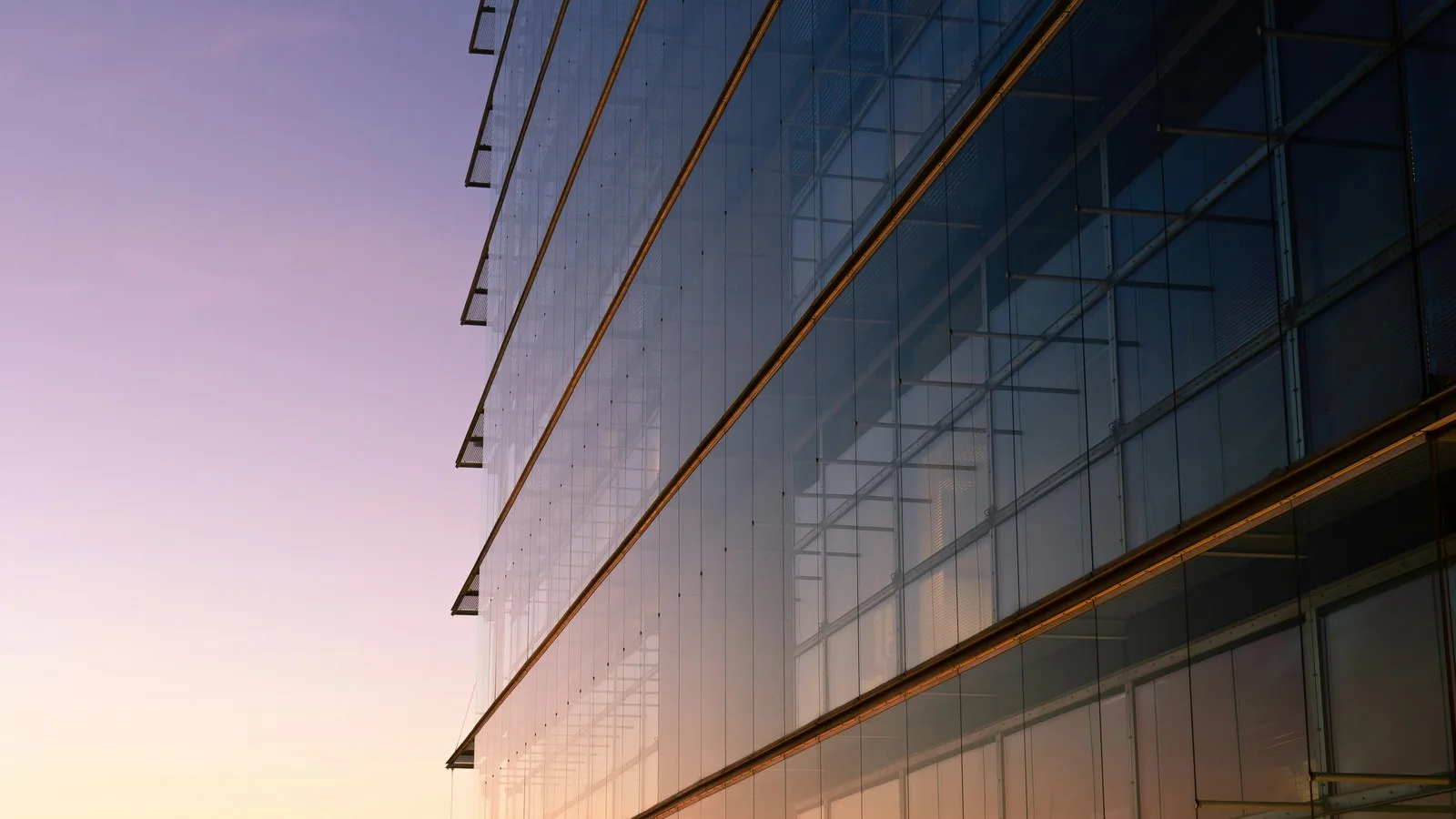 Looking up at a glass office facade with horizontal bands, lit in warm gold against a purple dusk sky